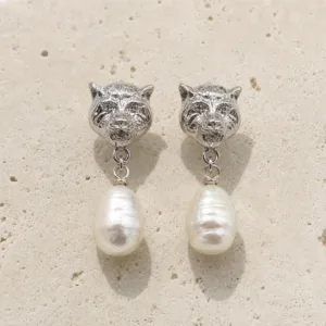 Brincos prateados com cabeças felinas e pérolas sobre pedra de tom quente