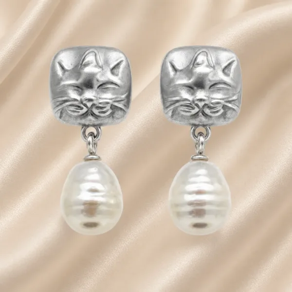Brincos prateados de gato com pérolas sobre cetim bege claro