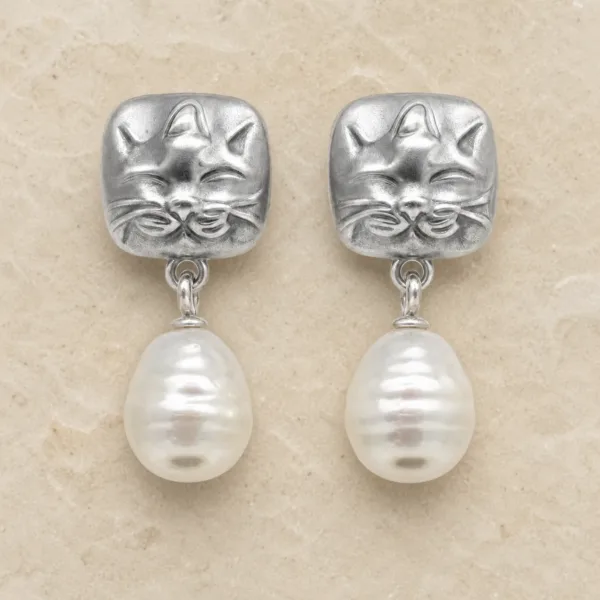 Brincos prateados de gato com pérolas sobre pedra de tom quente